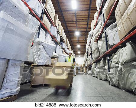 Stock Photo - Blurred view of Caucasian worker wheeling cardboard box in warehouse. Fotosearch