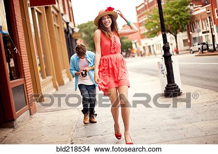 Picture - Boy photographing girlfriend on city sidewalk. Fotosearch