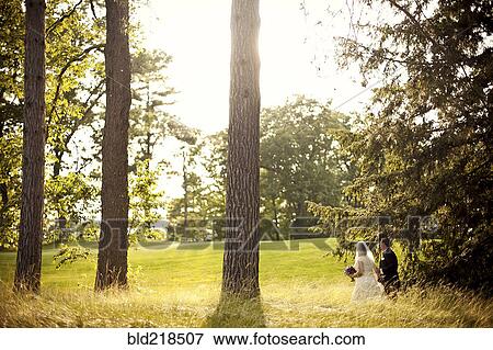 Stock Photo - Bride and groom walking in rural field. Fotosearch