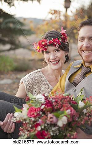 Stock Photograph - Bride carrying groom and bouquet in rural field. Fotosearch