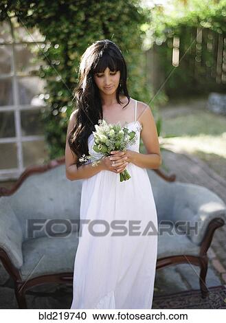Stock Image - Bride holding bouquet of flowers in backyard. Fotosearch