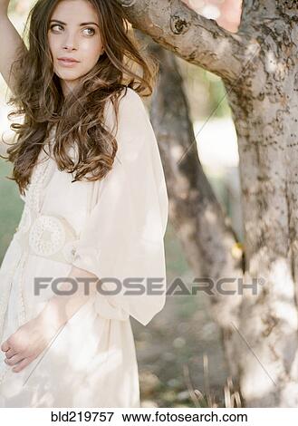 Stock Photo - Bride in wedding dress standing under tree. Fotosearch