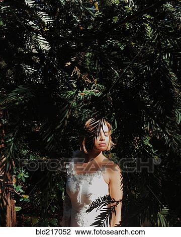 Stock Image - Bride wearing wedding dress under tree branches. Fotosearch