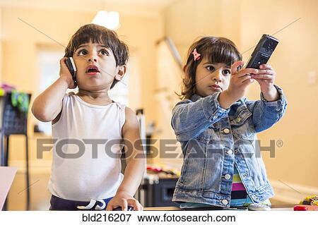Stock Photo - Brother and sister playing with cell phone and remote control. Fotosearch
