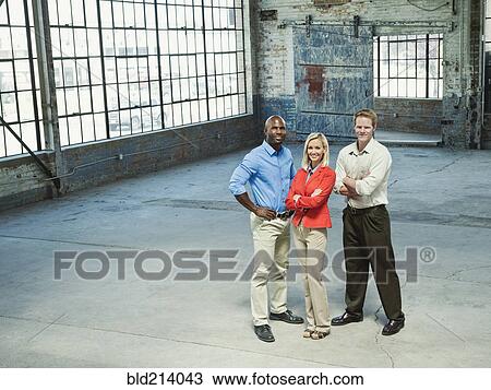 Stock Image - Business people smiling in empty warehouse. Fotosearch