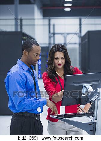 Stock Image - Business people using computer in server room. Fotosearch