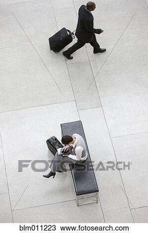 Stock Image - Business people with luggage in lobby. Fotosearch