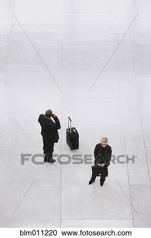 Stock Image - Business people with luggage standing in lobby. Fotosearch