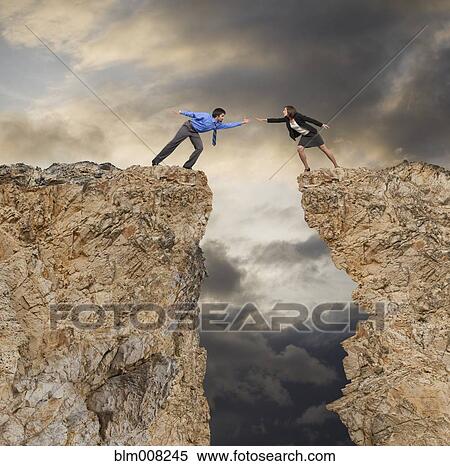Stock Photography - Businessman stretching to help co-worker across cliff gap. Fotosearch