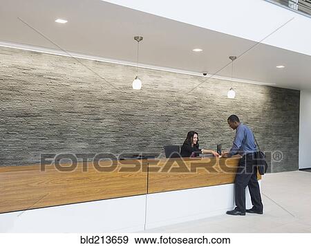 Stock Photo - Businessman talking to receptionist at office front desk. Fotosearch