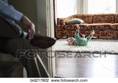 Businessman tying shoes as son plays in livingroom View Large Photo Image Stock Image - Businessman tying shoes as son plays in livingroom. Fotosearch
