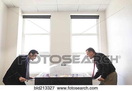 Businessmen playing foosball together in office View Large Photo Image Stock Photo - Businessmen playing foosball together in office. Fotosearch