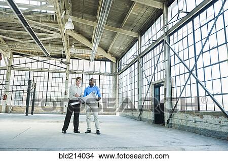 Picture - Businessmen reading blueprints in empty warehouse. Fotosearch