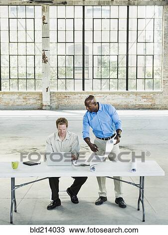 Businessmen reading blueprints in empty warehouse View Large Photo Image Stock Image - Businessmen reading blueprints in empty warehouse. Fotosearch