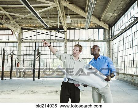 Stock Photography - Businessmen reading blueprints in empty warehouse. Fotosearch