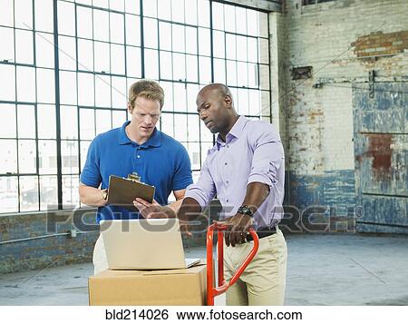 Stock Photograph - Businessmen using laptop on cardboard boxes in warehouse. Fotosearch