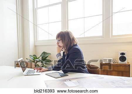 Stock Image - Businesswoman using laptop at desk in office. Fotosearch