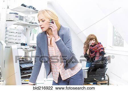 Stock Image - Businesswomen talking on cell phone in office. Fotosearch