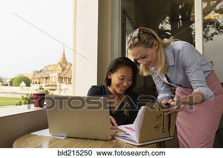 Stock Image - Businesswomen working together in cafe, Phnom Penh, Cambodia. Fotosearch