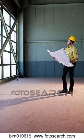 Stock Photography - Caucasian architect reviewing blueprints. Fotosearch