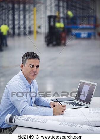 Stock Image - Caucasian architect working in warehouse. Fotosearch
