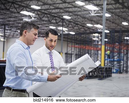 Stock Photograph - Caucasian architects reading blueprints in warehouse. Fotosearch