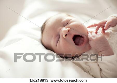 Stock Image - Caucasian baby girl yawning on bed. Fotosearch