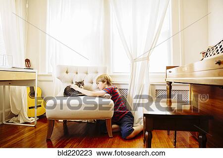 Stock Image - Caucasian boy petting cat in living room. Fotosearch