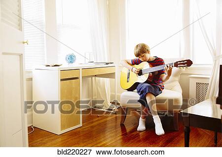 Stock Photo - Caucasian boy playing guitar in living room. Fotosearch