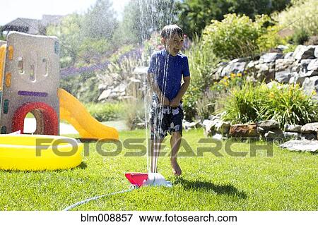 Stock Photo - Caucasian boy playing in backyard sprinkler. Fotosearch
