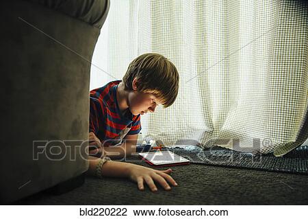 Stock Image - Caucasian boy using digital tablet in blanket fort. Fotosearch