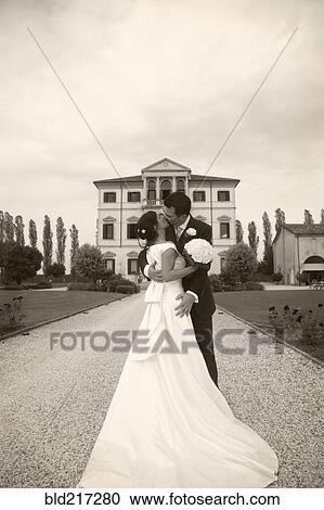 Stock Image - Caucasian bride and groom kissing on gravel path. Fotosearch