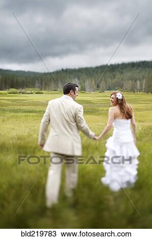 Stock Image - Caucasian bride and groom walking in rural field. Fotosearch