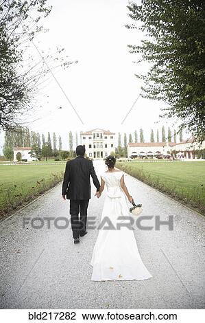 Stock Image - Caucasian bride and groom walking on gravel path. Fotosearch