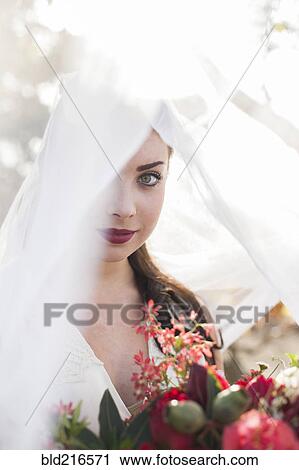 Stock Image - Caucasian bride holding bouquet under veil. Fotosearch