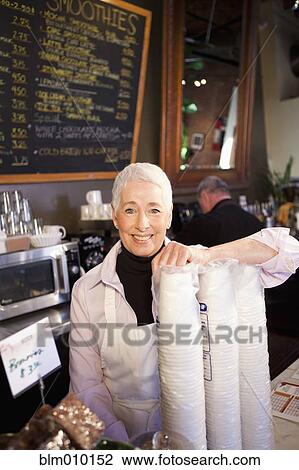 Stock Image - Caucasian business owner standing with disposable cups in cafe. Fotosearch