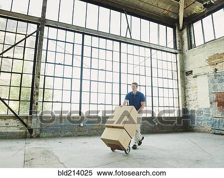 Stock Photography - Caucasian businessman pushing cardboard boxes on hand truck in warehouse. Fotosearch