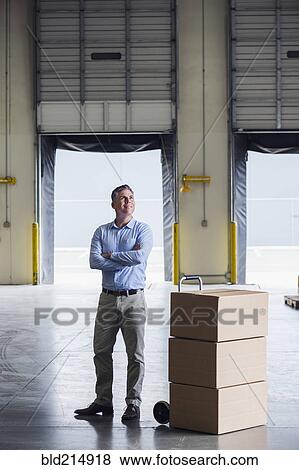 Caucasian businessman standing near cardboard boxes in warehouse View Large Photo Image Stock Photo - Caucasian businessman standing near cardboard boxes in warehouse. Fotosearch