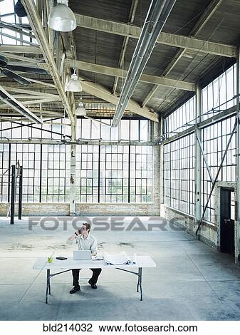 Stock Image - Caucasian businessman talking on cell phone in empty warehouse. Fotosearch