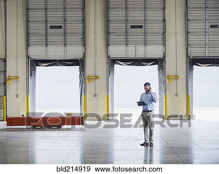 Stock Photo - Caucasian businessman talking on cell phone in warehouse. Fotosearch