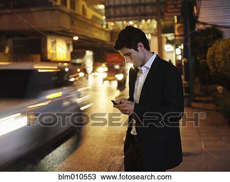 Stock Image - Caucasian businessman text messaging on cell phone outdoors. Fotosearch