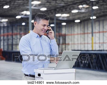 Caucasian businessman using laptop and cell phone in empty warehouse View Large Photo Image Stock Image - Caucasian businessman using laptop and cell phone in empty warehouse. Fotosearch
