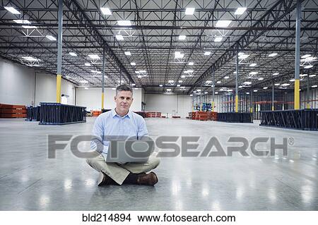 Picture - Caucasian businessman using laptop in empty warehouse. Fotosearch