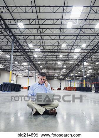 Stock Photography - Caucasian businessman using laptop in empty warehouse. Fotosearch