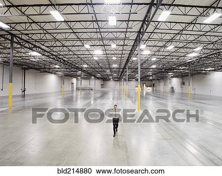 Stock Image - Caucasian businessman walking in empty warehouse. Fotosearch