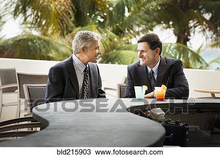 Stock Image - Caucasian businessmen with cocktails at patio bar. Fotosearch