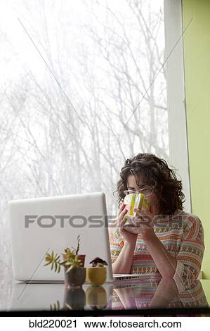 Stock Image - Caucasian businesswoman drinking coffee at desk. Fotosearch