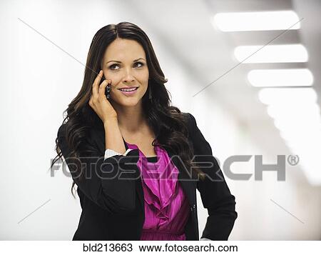Stock Image - Caucasian businesswoman talking on cell phone in office corridor. Fotosearch