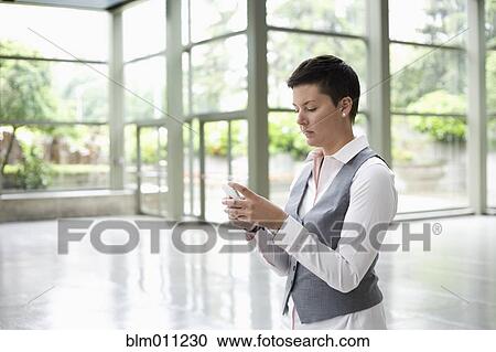 Stock Image - Caucasian businesswoman text messaging in lobby. Fotosearch