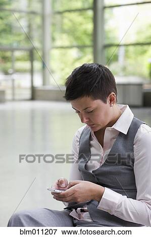Stock Photo - Caucasian businesswoman text messaging in lobby. Fotosearch